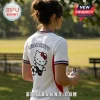 Woman wearing white Hello Kitty soccer jersey with red and blue trim, holding a metal water bottle in a park.!