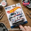 Hot Wheels 1/10 scale EMS ambulance die-cast vehicle in branded blister packaging on a wooden workbench surface.!
