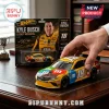 Kyle Busch M&Ms Toyota Camry diecast car held in hand with original blister pack packaging visible in the background.!
