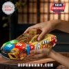 Toyota Camry M&Ms stock car themed glass whiskey decanter with gold cap held by two hands on a wooden table.!