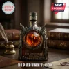 Eye of Mordor anniversary bottle with dark metallic frame, amber liquid, and inscribed text on a wooden desk with books.!