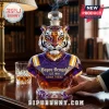 Faceted glass tiger head decanter in purple and gold with Bayou Bengals text on a wooden desk with a whiskey glass.!