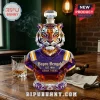 Faceted glass tiger decanter wearing purple and gold jersey with Bayou Bengals text on a wooden table with whiskey glass.!