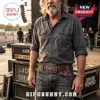 Man wearing a brown leather belt with a metal Lynyrd Skynyrd skull and wing belt buckle standing near stage equipment.!