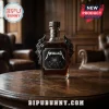 Metallica branded glass whiskey bottle with ornate metal wings on a wooden table in a dimly lit library setting.!