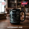 Black ceramic coffee mug featuring Metallica logo, skull, chains, and white crosses graphic on a wooden office desk.!