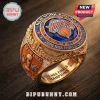 Gold 2026 New York Knicks championship ring featuring a blue stone, orange crystals, and team logos on a wooden background.!