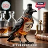 Raven-shaped glass whiskey bottle with Old Crow bourbon label, standing on a wooden desk with clear decanters in background.!
