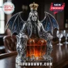 Ozzy Osbourne shaped silver decanter with bat wings, skull armrests, a gold crown, and amber whiskey on a wooden bar.!