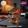 Snoopy-shaped glass whiskey decanter wearing aviator goggles and a red scarf filled with amber liquid on a dark desk.!
