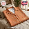 Orange button-down short-sleeve shirt with repeating teal and yellow diamond ikat patterns folded on a beige bed.!