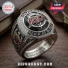 Slayer band championship style ring with red and silver logo, black stone, and engraved text on a wooden surface.!