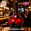 Decorative red glass decanter with black ornate filigree base and crown topper sitting on a wooden bar table.!