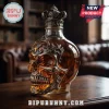 Skull-shaped glass decanter filled with amber liquid, featuring metallic ornate filigree and a matching decorative stopper.!
