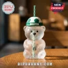 Starbucks bear-shaped clear glass cup with a green and white soccer ball lid and matching striped straw on a wooden table.!
