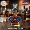 Superman bust-shaped glass whiskey decanter with red, blue, and yellow painted emblem details on a wooden bar surface.!