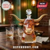 Faceted glass whiskey decanter shaped like a bull head with gold horns and an 1893-2026 anniversary plaque on a wood table.!