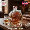 Predator helmet shaped glass decanter filled with amber liquid, featuring red accents, sitting on a wooden desk with glass.!