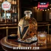 Gold metallic helmet-shaped whiskey decanter labeled The Golden Misfits 2017-2027 with matching glass on wooden table.!