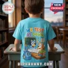 Child wearing a light blue t-shirt with Bluey characters, books, and text reading We Test At Dawn on the back.!