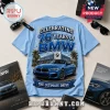 Light blue t-shirt with BMW 76th anniversary graphic featuring a blue coupe, dealership, and fireworks design.!
