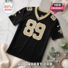 Black New Orleans Saints jersey featuring gold numbers 89 and fleur-de-lis logos on a white marble and concrete surface.!