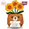 Crocheted brown bear holding a sign with yellow sunflower bouquet, dark eyes, and white snout on a white background.!