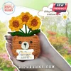 Crocheted brown bear holding a sign with yellow sunflowers in a pot held by human hands.!