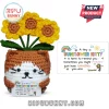 Crocheted brown and white cat holding a note with three yellow sunflowers attached to its head on a white background.!