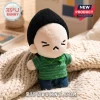 BTS Min Yoongi Grumpy Face Plush Doll wearing a black beanie and green striped polo shirt sitting on a beige knit throw.
