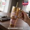 BTS x BT21 Cosmic Friends gold stainless steel tumbler with handle, straw, and cartoon character graphics on desk.
