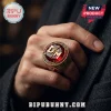 Depeche Mode Enjoy The Silence gold ring featuring a deep red center stone and DM lettering worn on a person's finger.