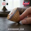 Gold championship ring featuring blue gemstone border, 1872 engraving, and London landmarks on a wooden table.!