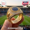 FIFA World Cup 2026 Gold Championship Ring featuring blue gemstone center, diamond accents, and soccer trophy side detail.