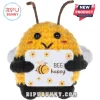Yellow and black crochet bumblebee plush holding a white sign with floral graphics and the text BEE happy.!