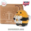 Crochet bee plush toy holding a sign that reads Bee happy in front of a cardboard gift box with heart icons.!