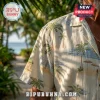Cream-colored short-sleeve button-down shirt with vintage beach, palm tree, and tiki hut print worn outdoors.!