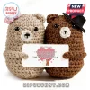 Two crochet bears holding a card with a love quote and bear illustration, one wearing a pink bow and one a black hat.!