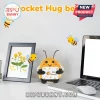 Crocheted yellow and black bee plush holding a white card printed with Bee Yourself text on a desk near a laptop.!