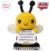 Crocheted yellow and black bee plush holding a white sign with black text about kindness and stinging. White background.!