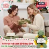 Two women exchanging a green gift box next to a birthday cake and a small green crocheted turtle holding a birthday card.!
