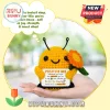 Small yellow crochet bee plushie with black antennae holding an orange flower and a positive message card in a hand.!