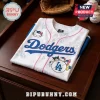 White LA Dodgers baseball jersey featuring Hello Kitty and Sanrio character graphics with pink trim on a wooden table.!