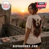 Woman wearing a cream t-shirt with a dragon and crown graphic on the back against a backdrop of a medieval castle at sunset.!