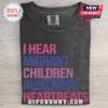 Human Rights Migrant Children Heartbeats T-Shirt in charcoal grey with pink and blue text on a wooden surface.