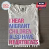 Human Rights Migrant Children Heartbeats T-Shirt in white cotton with pink and blue block lettering on wood background.
