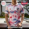 Pink polo shirt featuring Japan flag, JFA crest, and cherry blossom patterns with mountain silhouettes on white background.!