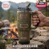 Olive green Jeep Legacy travel mug with 3D grille, tire base, and 85-year anniversary text held outdoors by a campfire.!