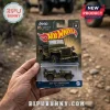 Hot Wheels Jeep 85th Anniversary Willys MB die-cast toy in olive green blister packaging held against a dirt road background.!