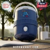 Blue plastic beverage cooler with white handle, spigot, and a bell graphic logo on an outdoor wooden table.!